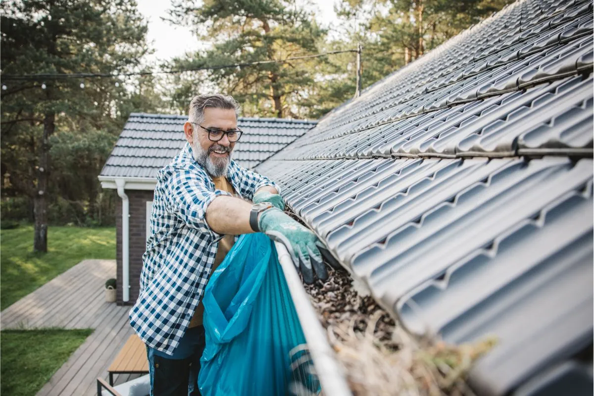 man cleaning leaves from gattering of house